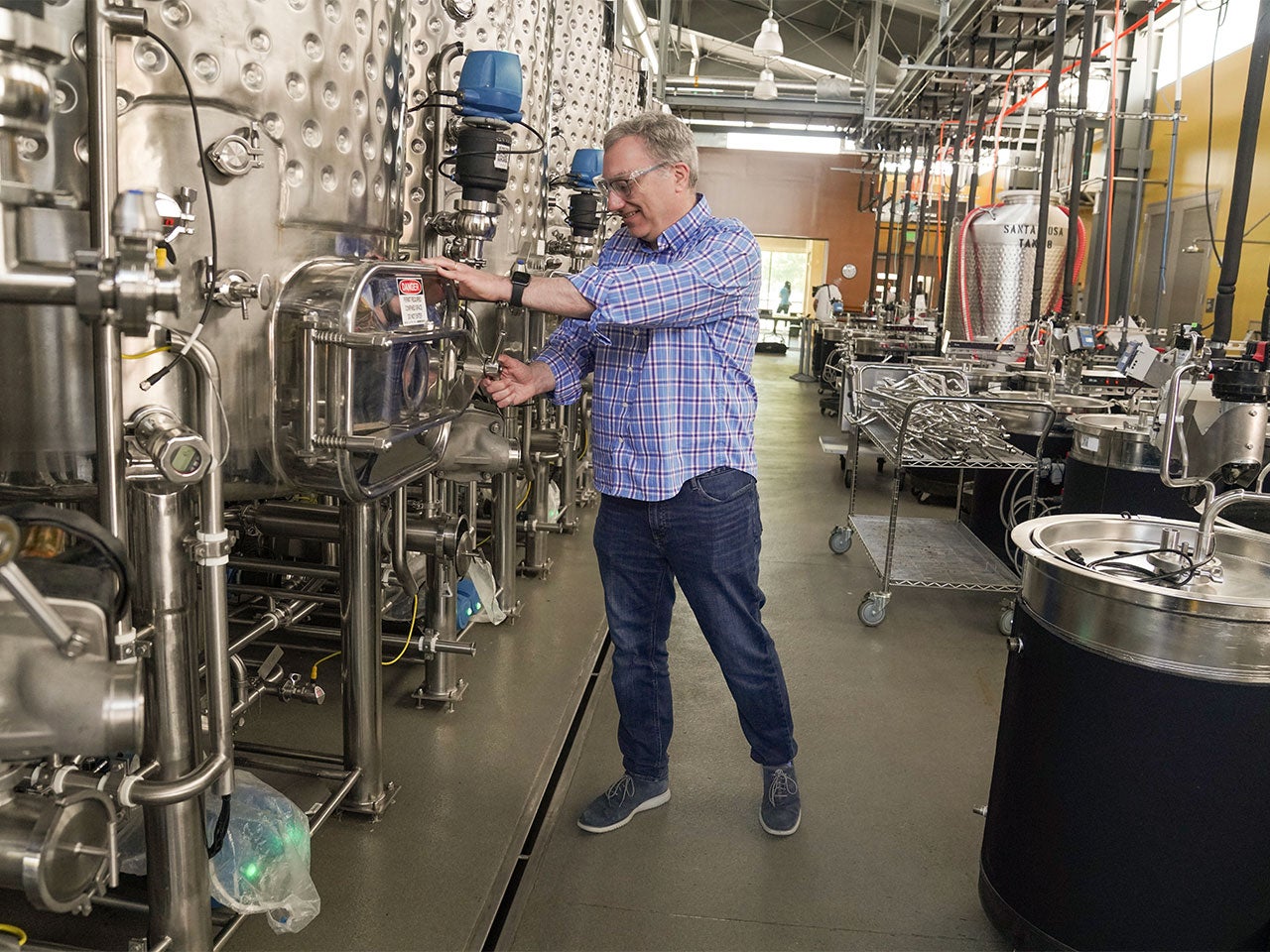 David Block, wearing safety goggles, demonstrates how to open a valve on a large fermentation tank.