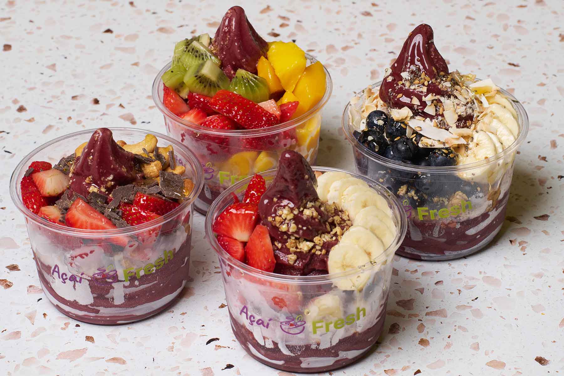Four clear-cup fruit and yogurt parfaits with berries, banana, mango, granola