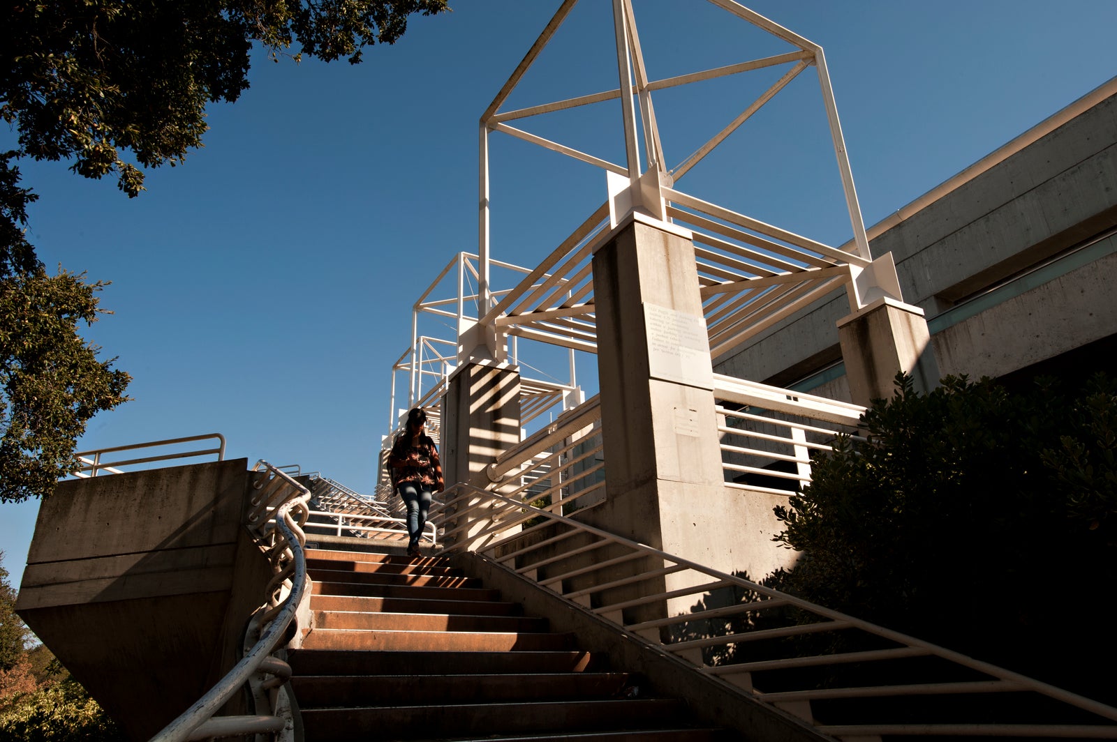 A woman walks down a staircase outside a parking structure.