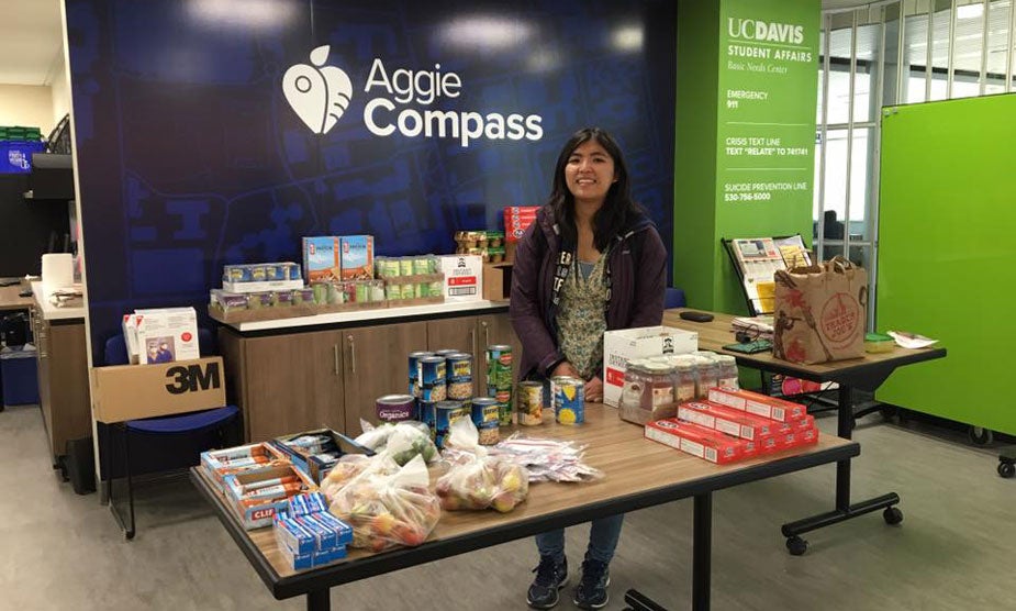 Woman stands at table offering food, at Aggie Compass.