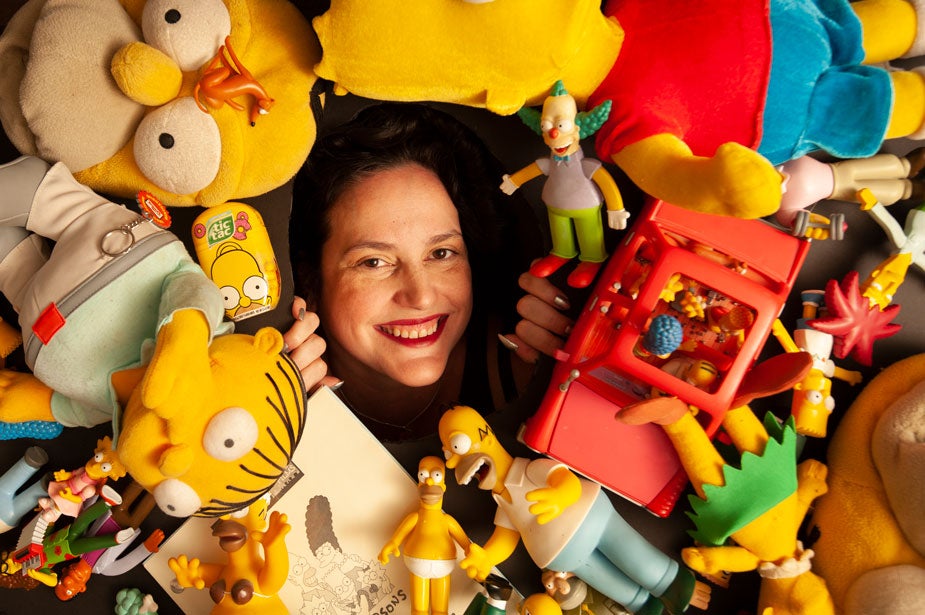 Karma Waltonen's head pokes through hole in a board covered with "The Simpsons" cartoon toys.