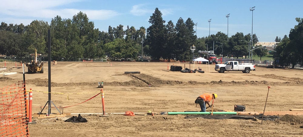 Workers lays pipeline on practice field.
