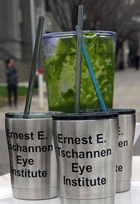 Blender container filled with kale smoothie, standing next to "Ernest E. Tschannen Eye Institute" cups.