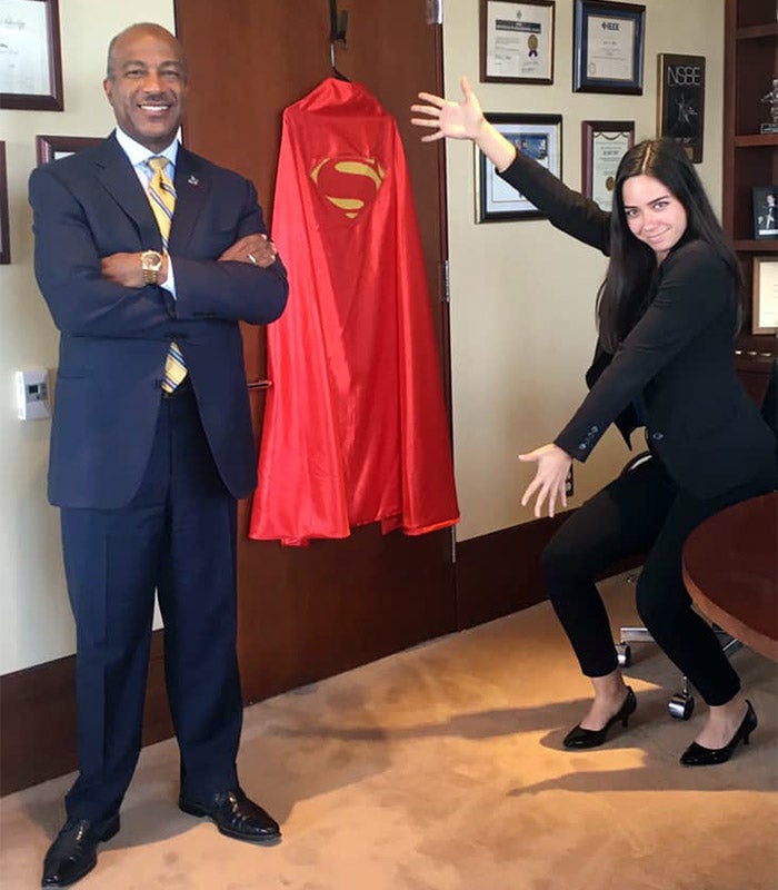Student Teddy Cruz poses for a photo with Chancellor Gary S. May and a Superman cape.