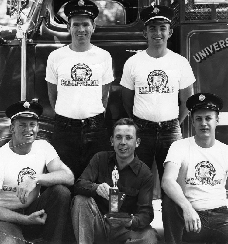Firefighters pose with trophy, in front of firetruck.