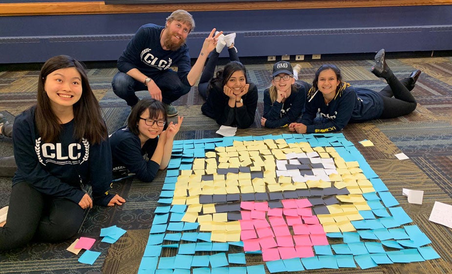 Students surround mural made from Post-it notes.
