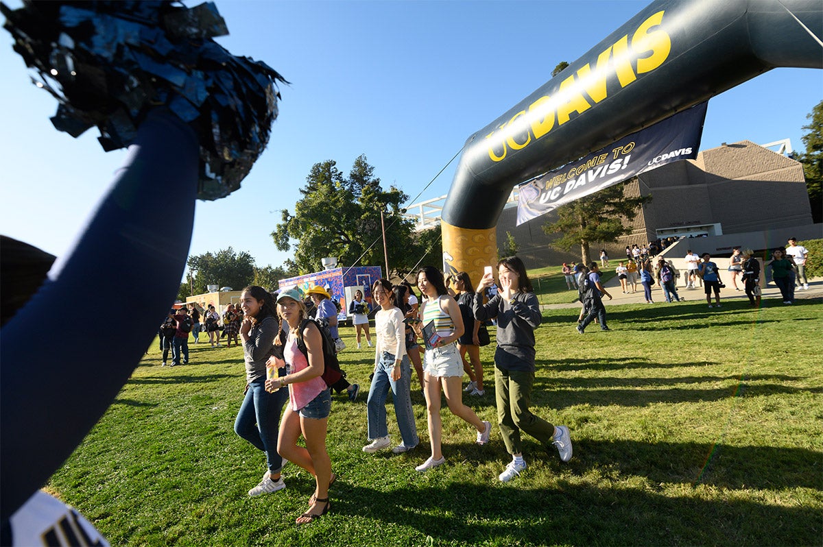 Students walk under a "Welcome to UC Davis" archway.