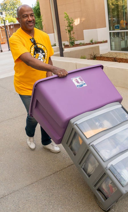 Chancellor p;ushes a handcart loaded with a student's belongings.