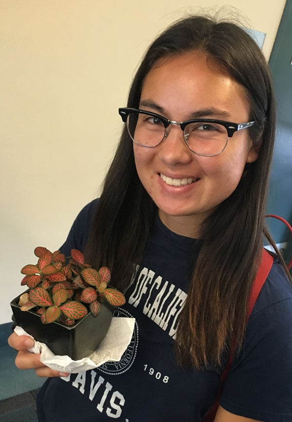 Student smiles while holding a plant.