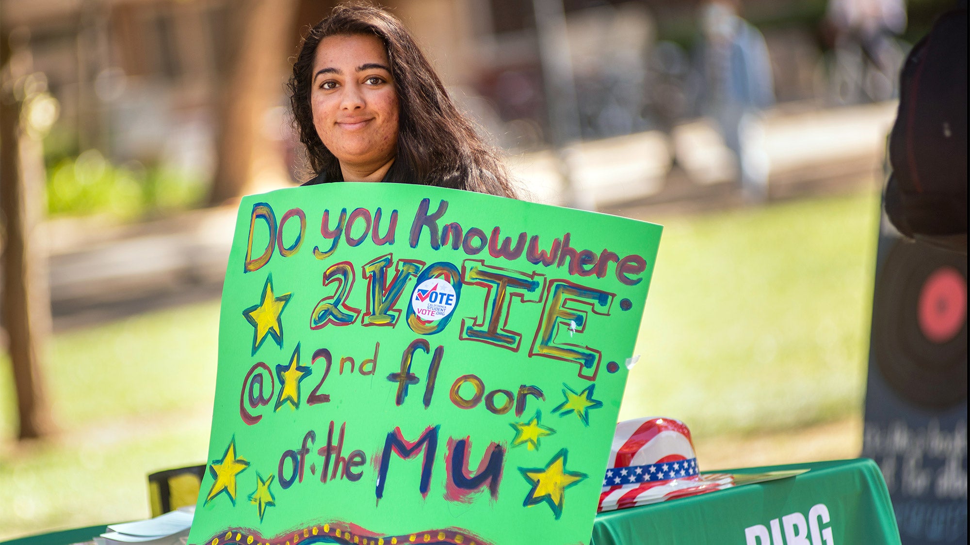 Student holds sign reading "Do you know where 2vote? @ 2nd floor of the MU"