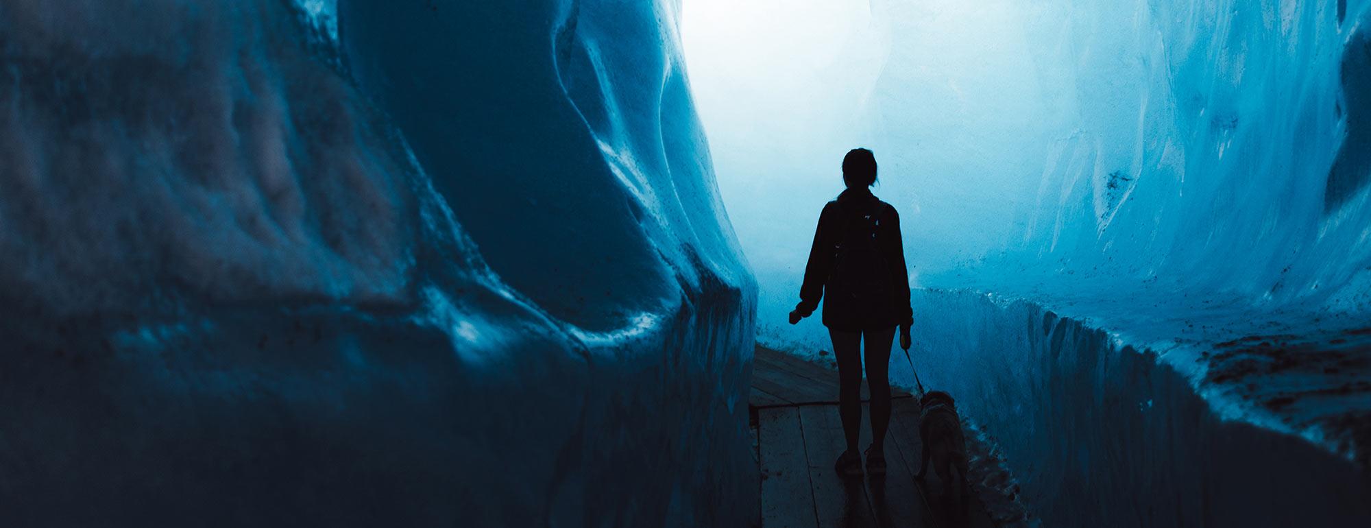 A silouette of a person walking into a glacier with her dog