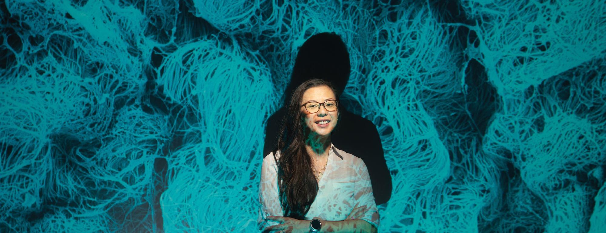 A female student smiles while being projected with an image of microscopic life
