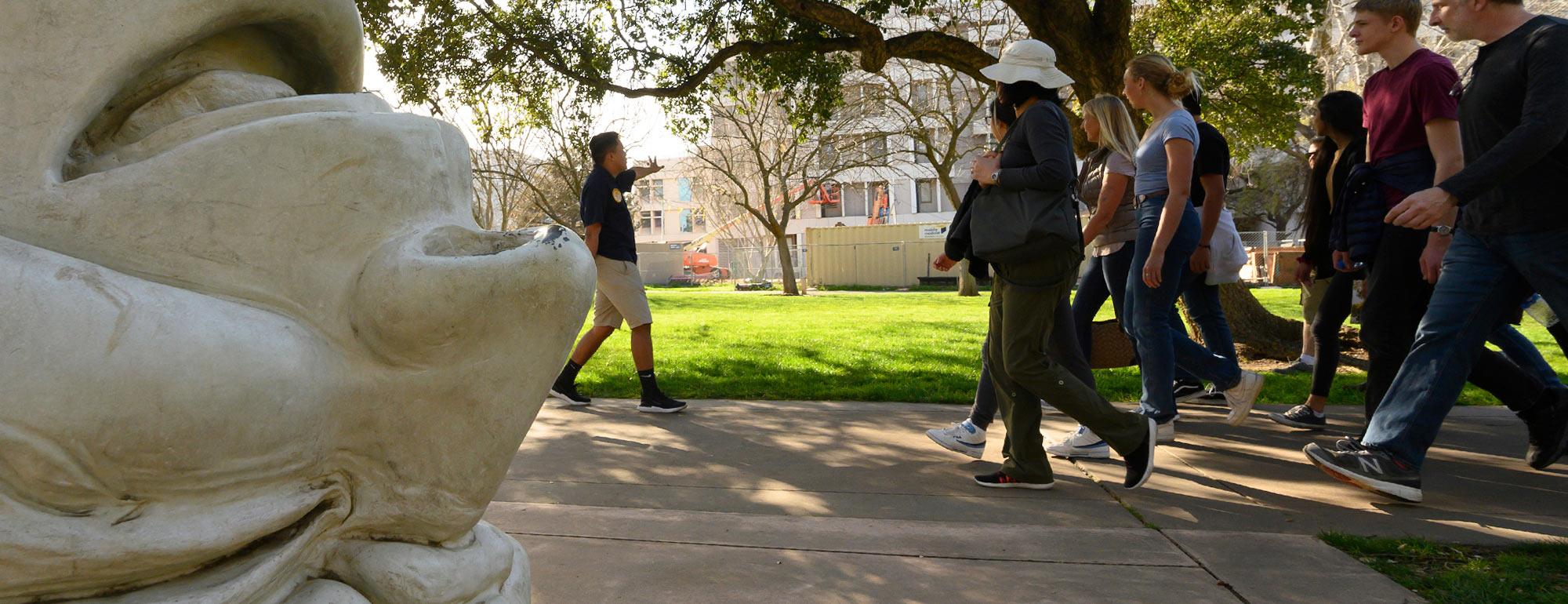 A student tour guide leads a walking tour past one of our unique egghead sculpture