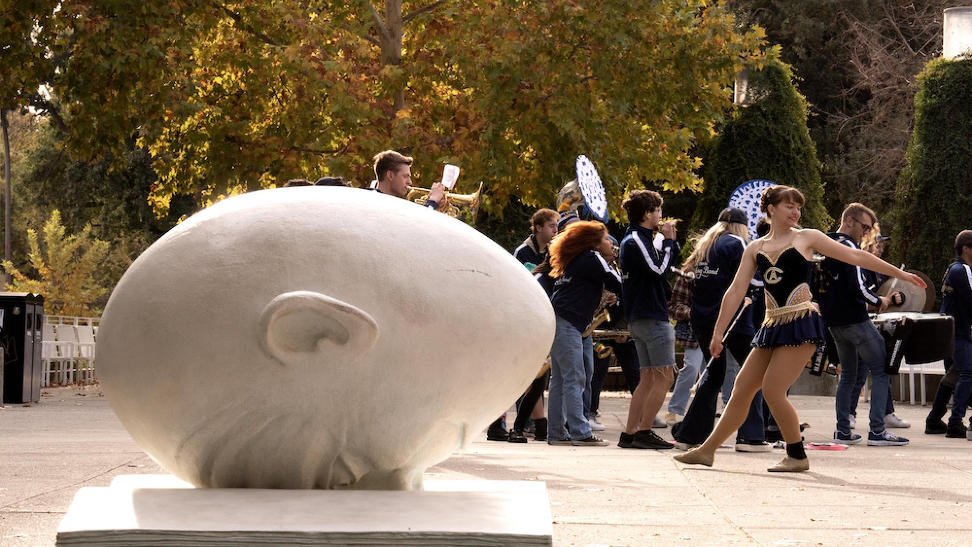 Bookhead egghead sculpture in fall with a band performing in the background