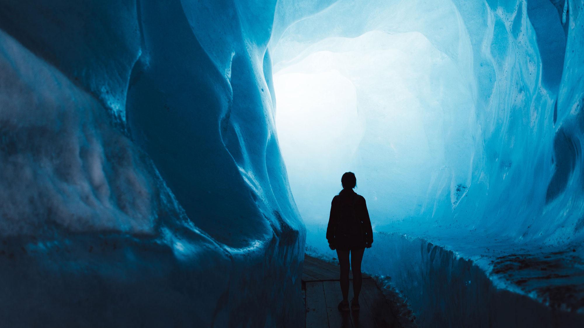 A lone young woman stands in an ice cave