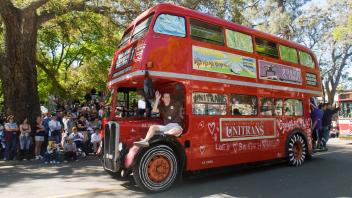 A red double decker bus rolls through campus during the Picnic Day parade