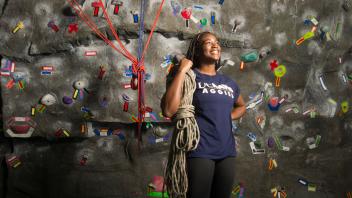 student standing in front of a rock climbing wall.