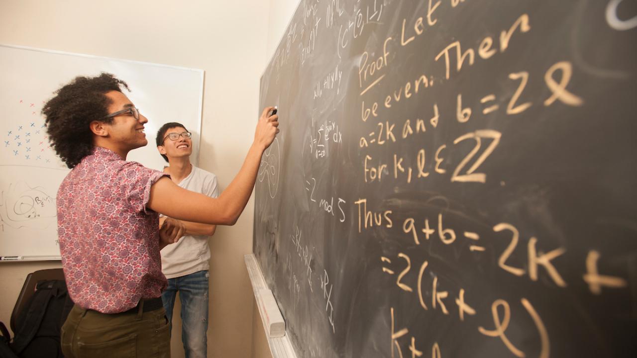 A student writes equations on a chalkboard covered with math. 