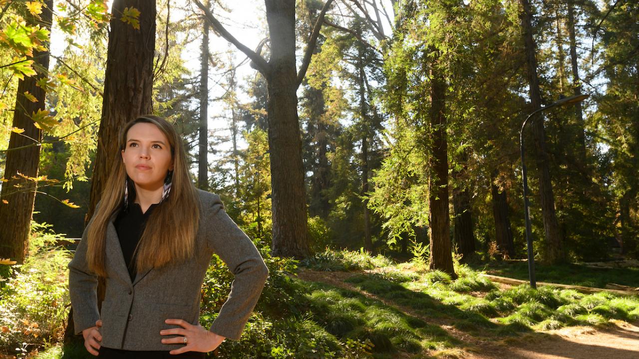 Erica stands with her hands on her hips in the tree-lined arboretum of UC Davis. 