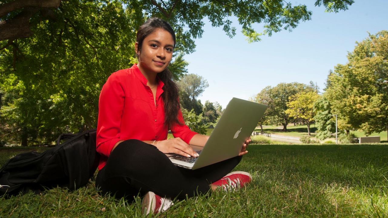 A student sits in the grass cross-legged with her laptop in 2017. 