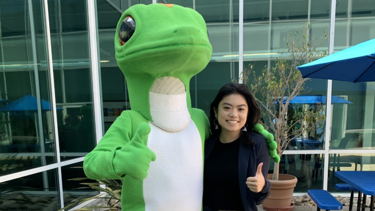 A sociology major gives a thumbs up as she poses with a person in a Geico Gecko suit. 