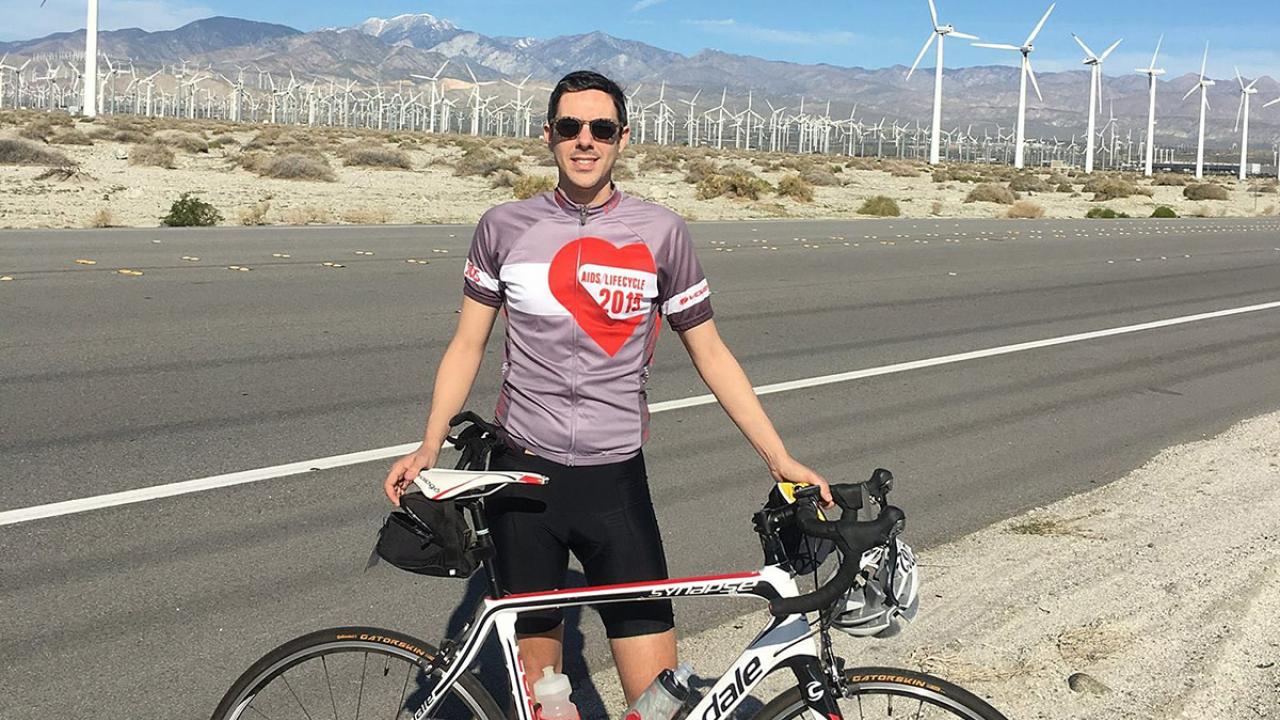 International relations graduate Tim Mizrahi poses with a road bike next to a highway with windmills in the background