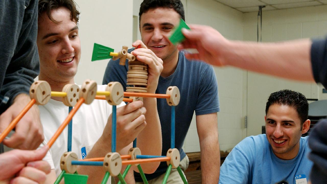 A team of male students using Tinketoys to build a structure