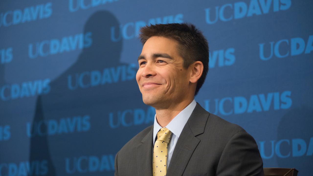 Intercollegiate Athletics Director Kevin Blue smiles in front of a UC Davis backdrop.