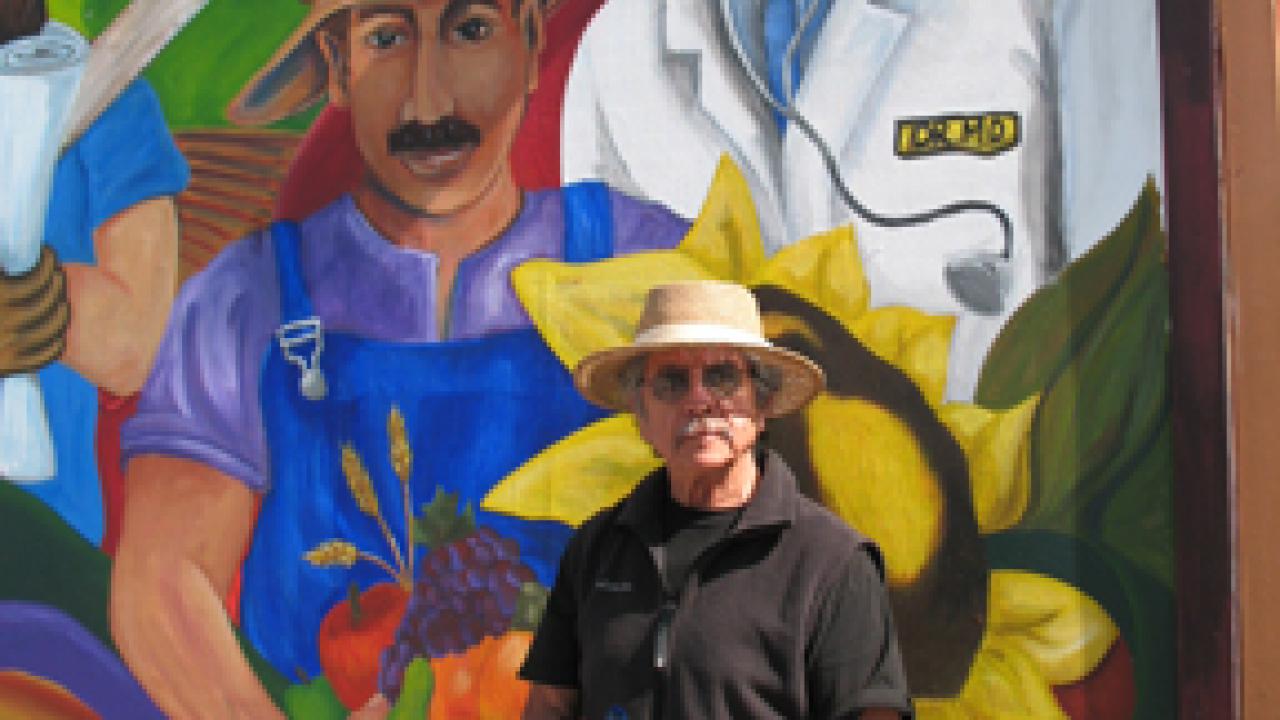 Professor Malaquias Montoya poses in front of his new mural at Beamer Park Elementary School in Woodland.