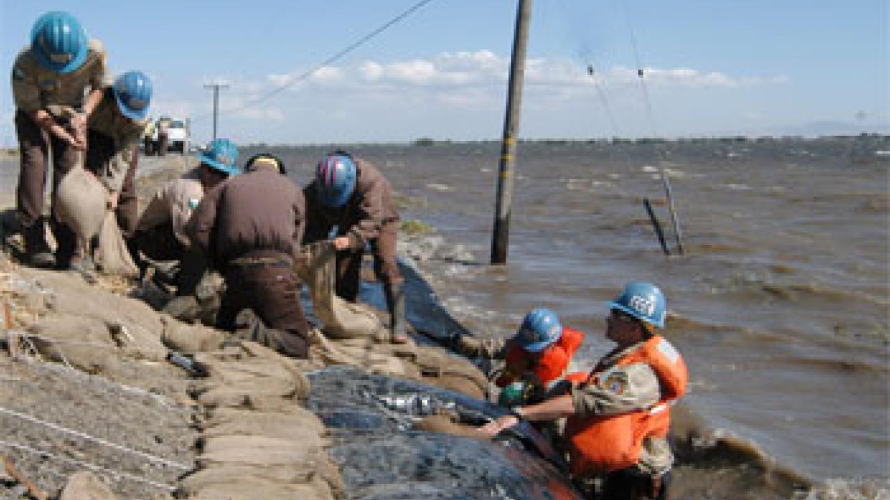 photo: people in hardhats filling sandbags and standing in water