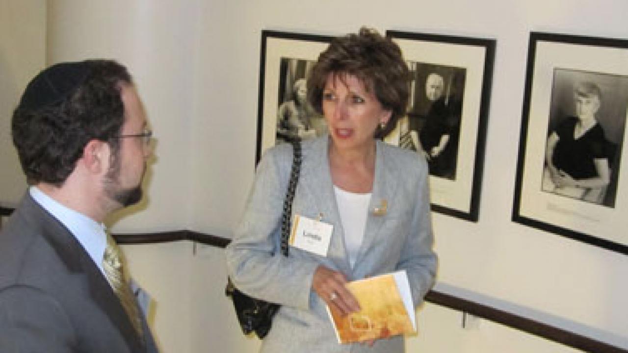 Chancellor Linda Katehi chats with Mark Katrikh of the Museum of Tolerance against a backdrop of photos of Holocaust survivors.