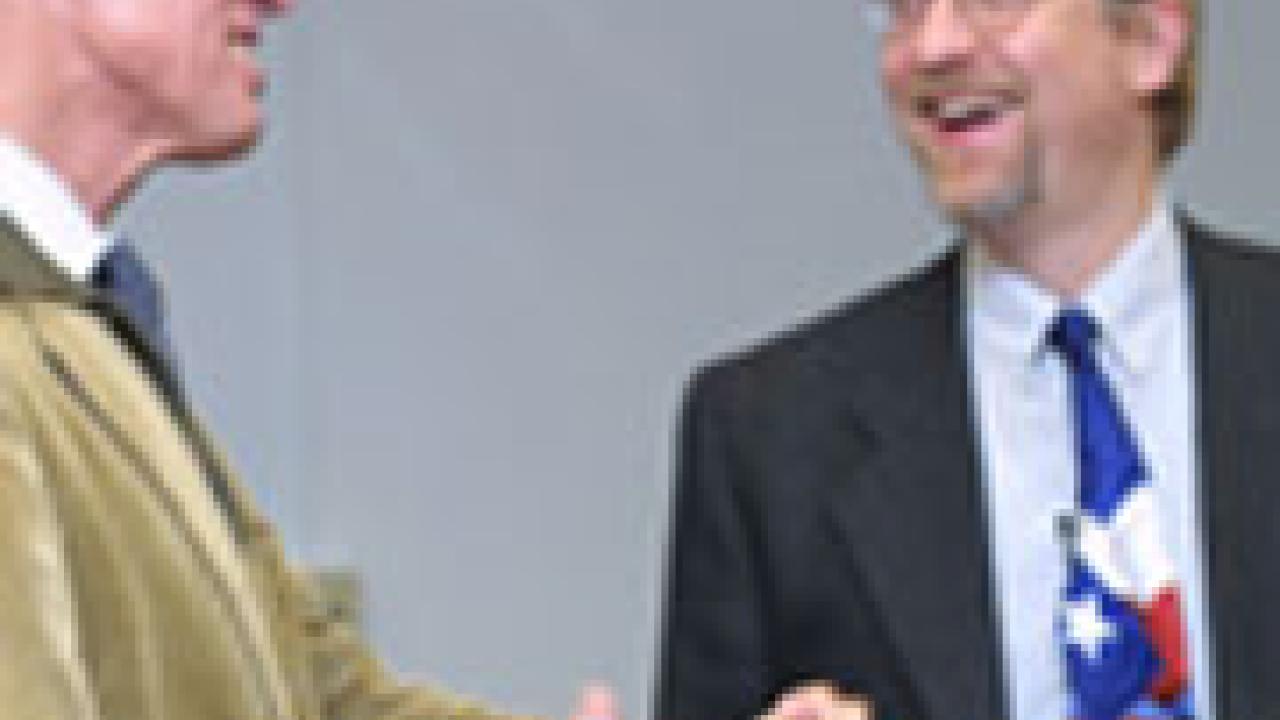In a photo, two men stand laughing.