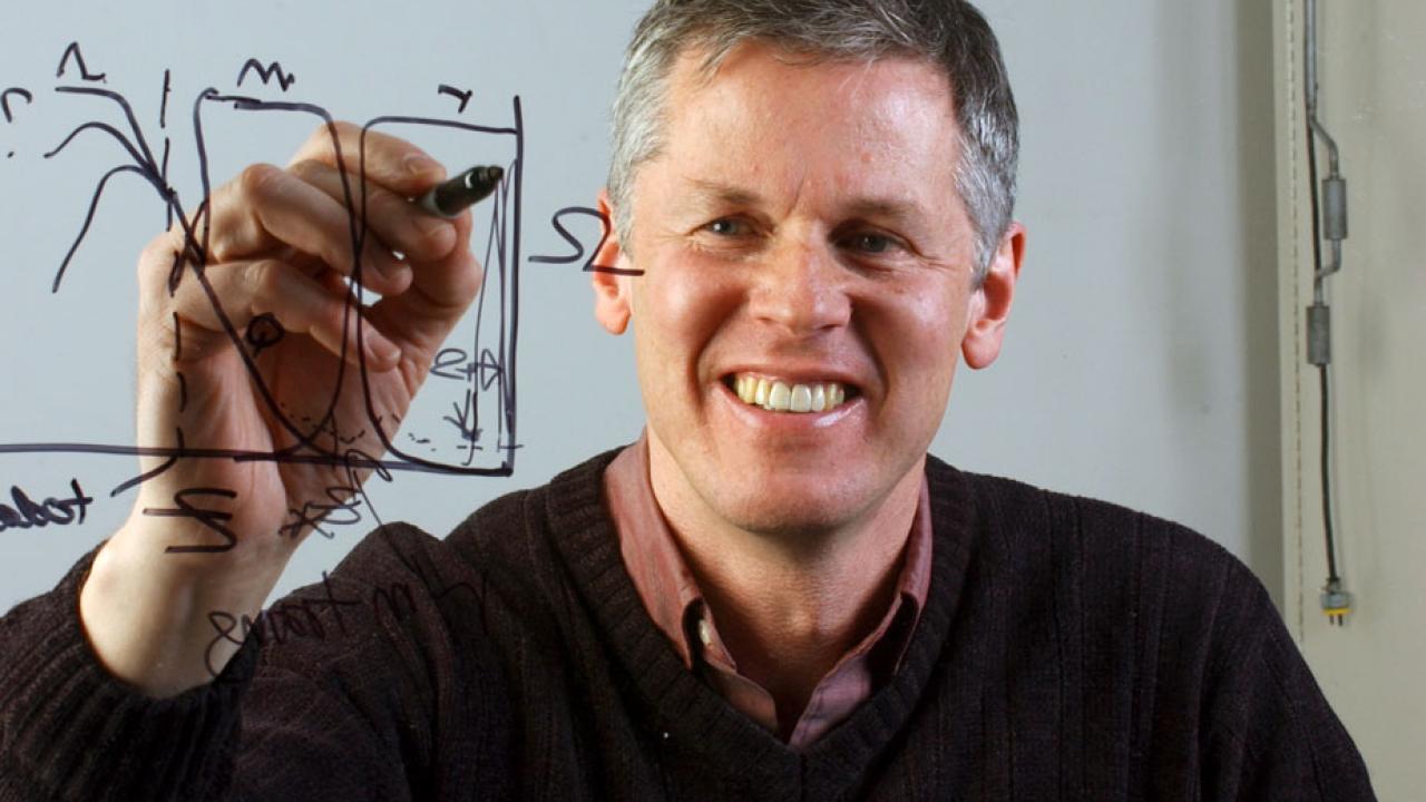 Professor Andy Albrecht, facing camera, through translucent "chalk" board.