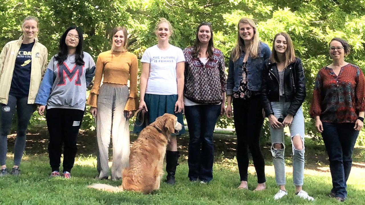 Assistant Professor Gwen Arnold, flanked by some of her students, in a line facing the camera, with Doug the Dog next to Gwen