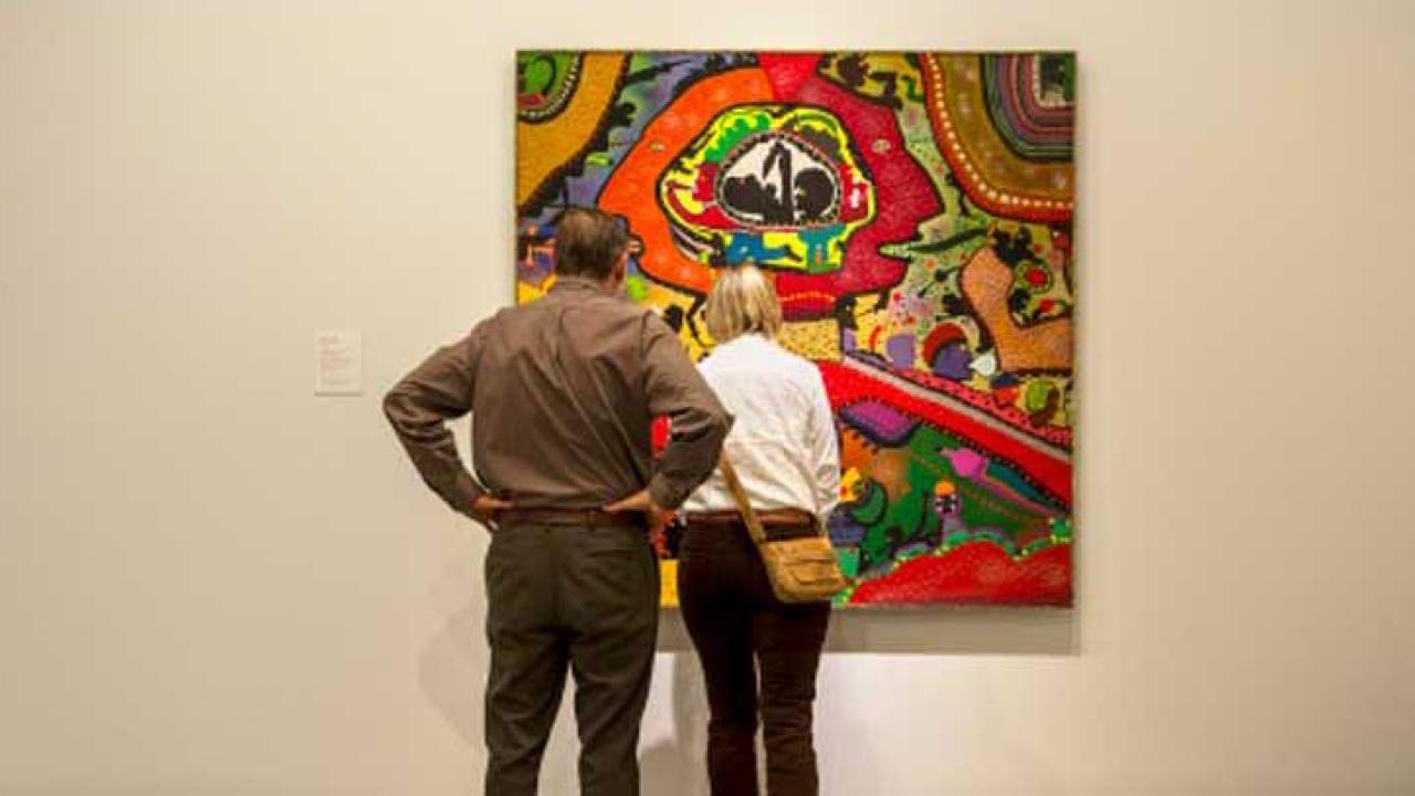 Two people viewing a framed work of art on wall.
