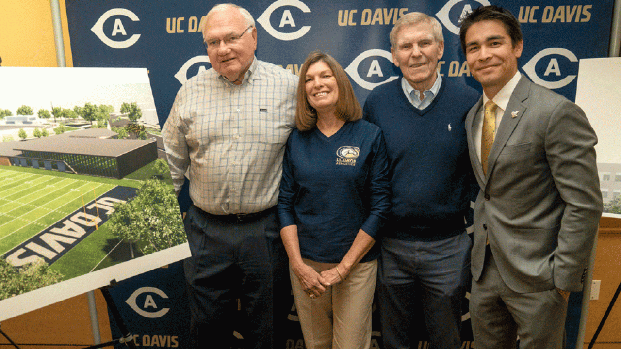 Donors and athletics difrector pose next to rendering of  Student-Athlete Performance Center and practice field,