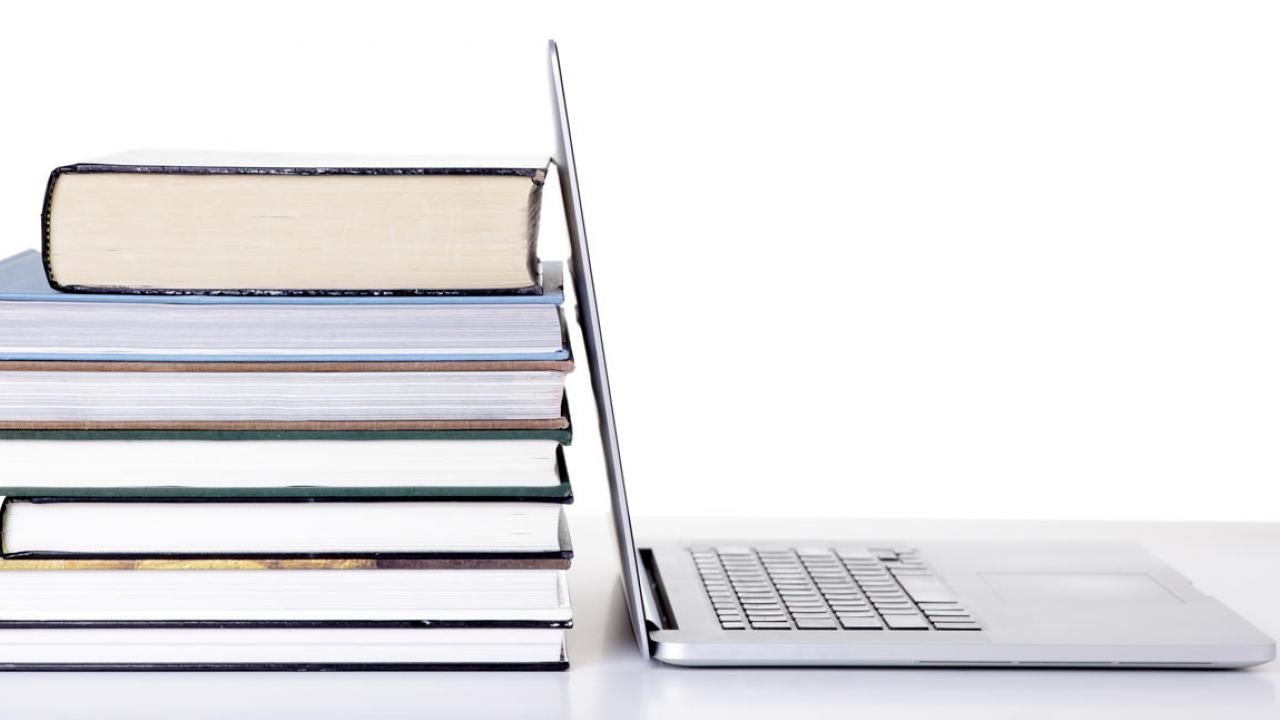 Stack of books next to an open laptop