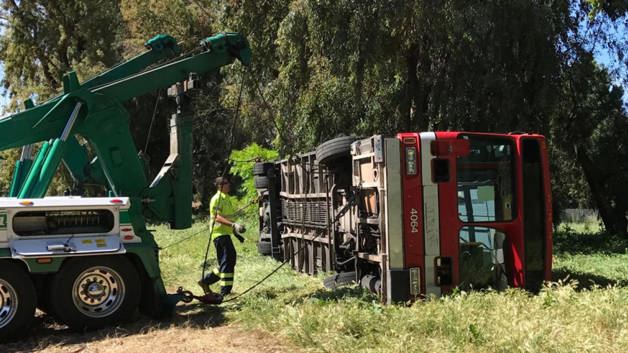 Tow truck tips old Unitrans bus onto its side, for training exercises.