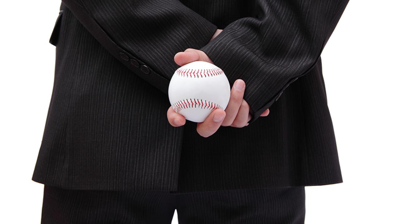 suited man holds a baseball behind him
