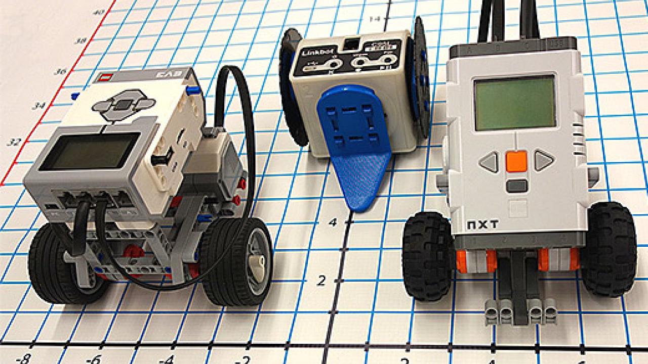 Three small robots, two on wheels, sitting on a paper grid