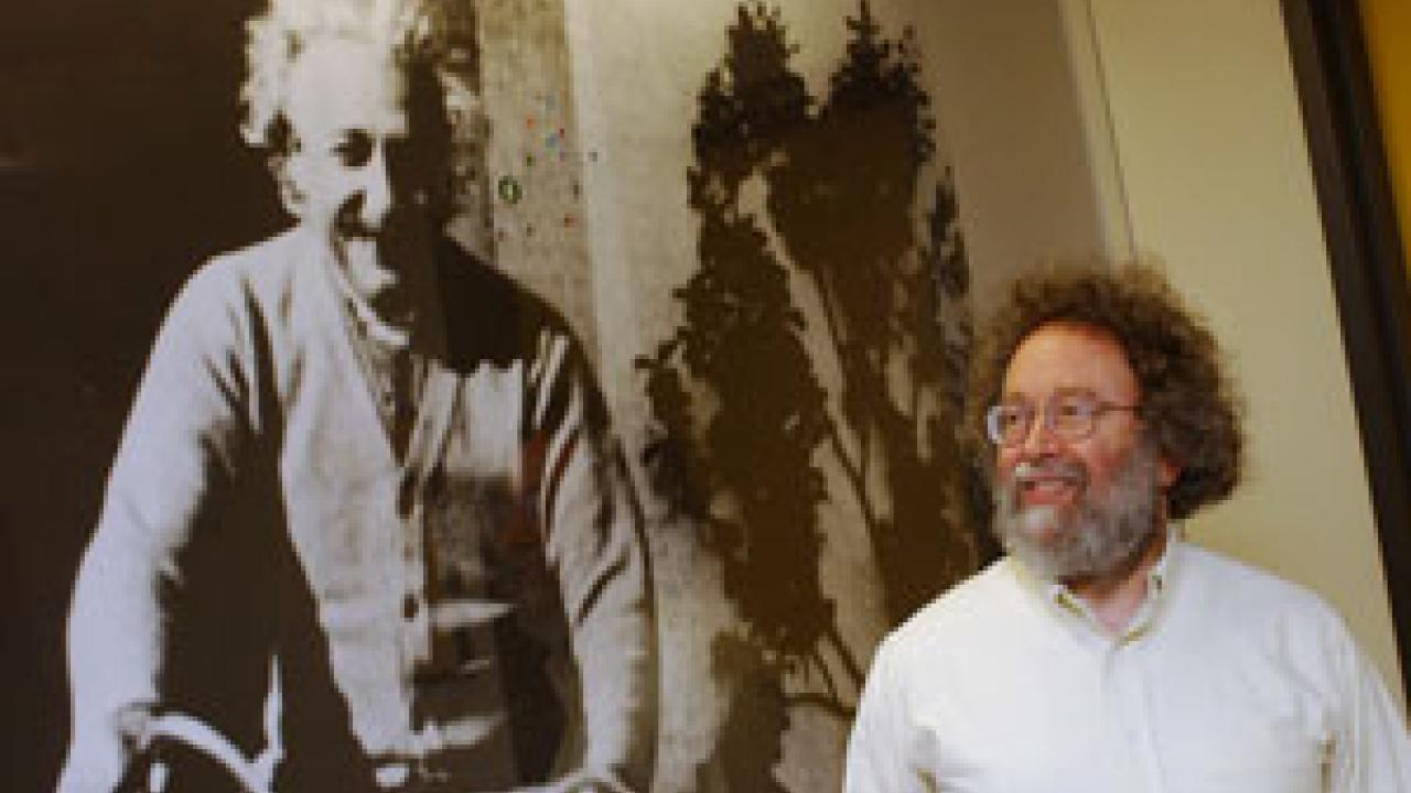 Physics professor Steve Carlip stands next to a bigger-than-life image in the Physics and Geology building of Albert Einstein riding a bike. Theories that Einstein published in 1905 have provided a catalyst for the work of Carlip and several oth