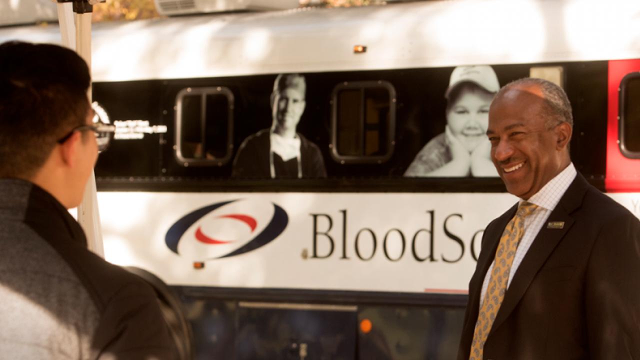 Chancellor chats with blood donors, in front of bloodmobile.