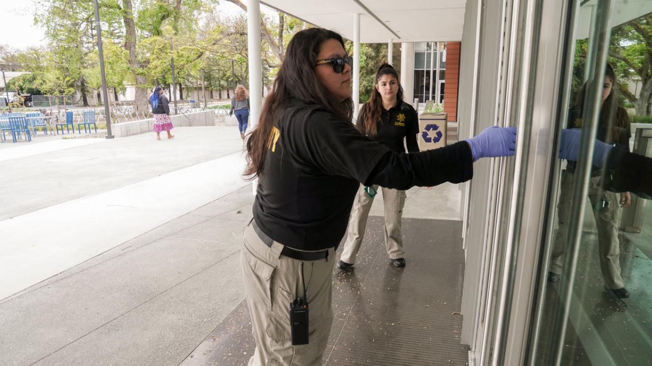 Two female Aggie Hosts, in uniform, checking doors to be sure they are locked.