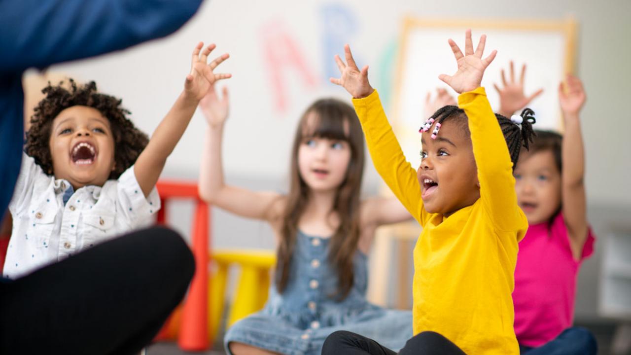 Children excitedly throw up their hands in child care.
