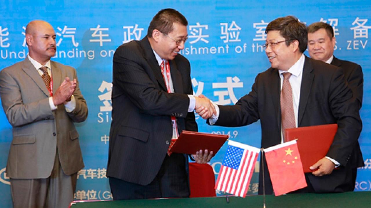 Two men in the foreground shaking hands with two men flanking them behind and sign in Chinese as background