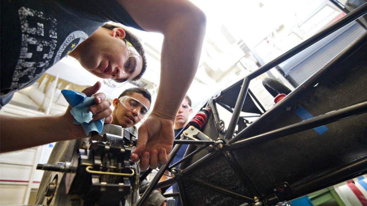 Three students adjust gears on a racecar frame that they designed