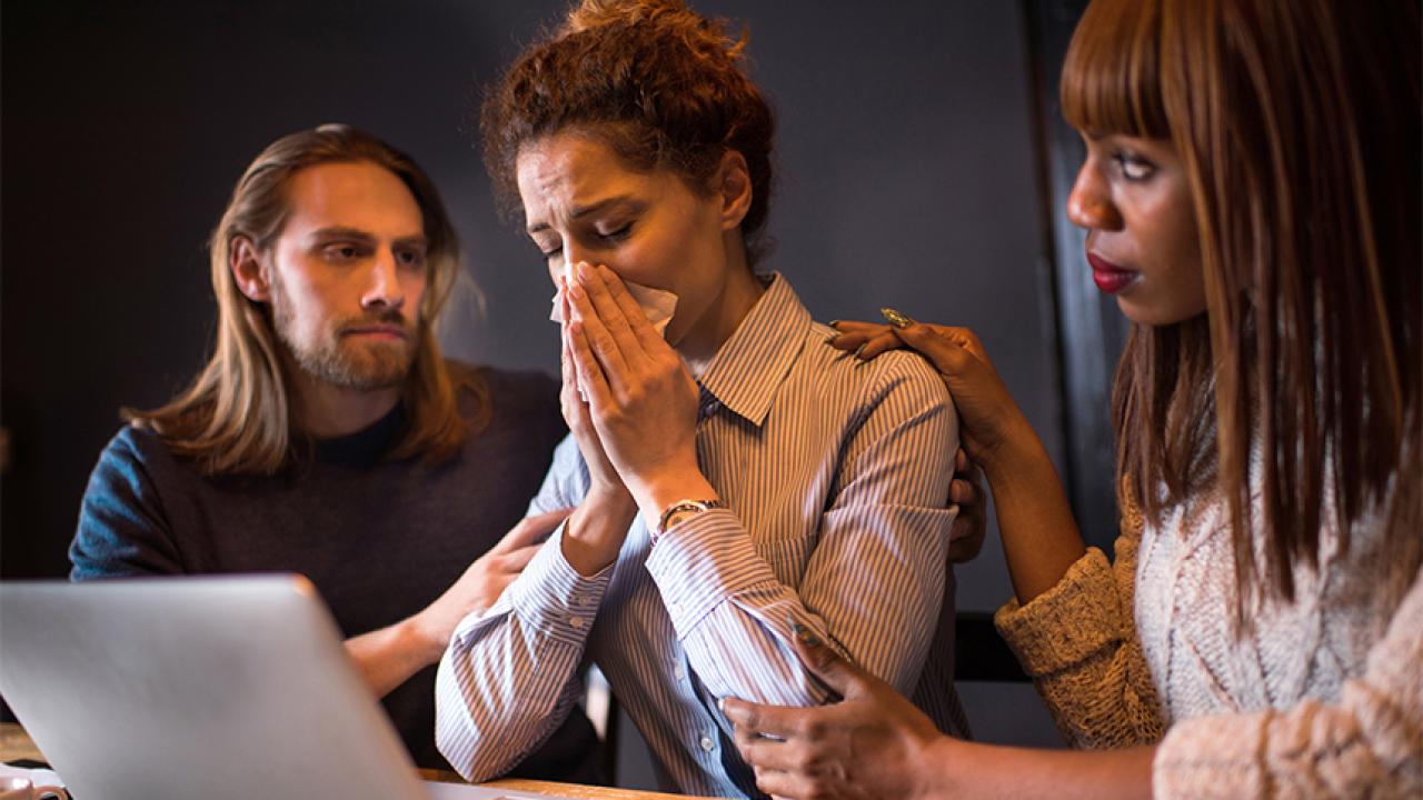 Two work colleagues comfort a crying woman 