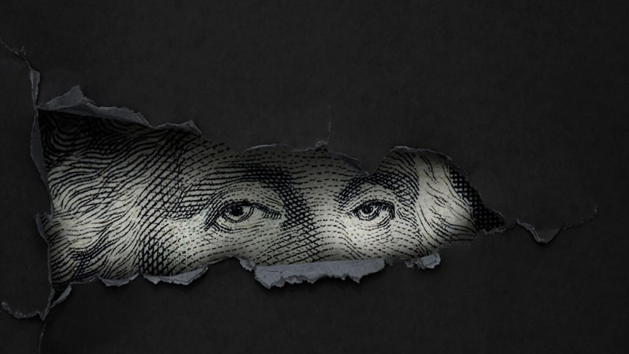 The eyes George Washington, as imprinted on a dollar bill, peer through a hole ripped in a dark material