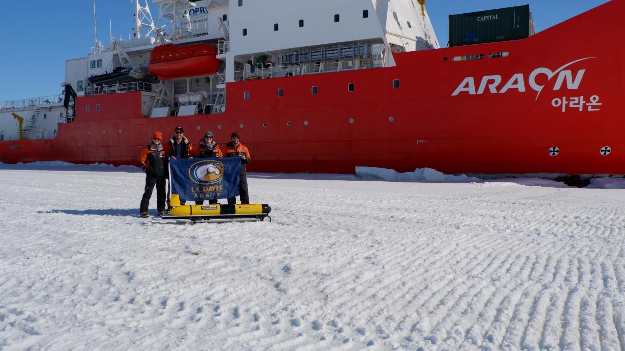 Scientist with glider and flag in front of icebreaker on top of ice