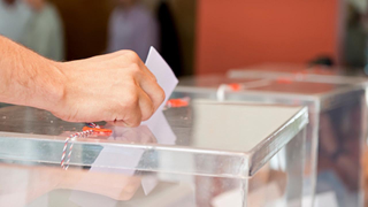 Hand placing ballot into a clear plastic box